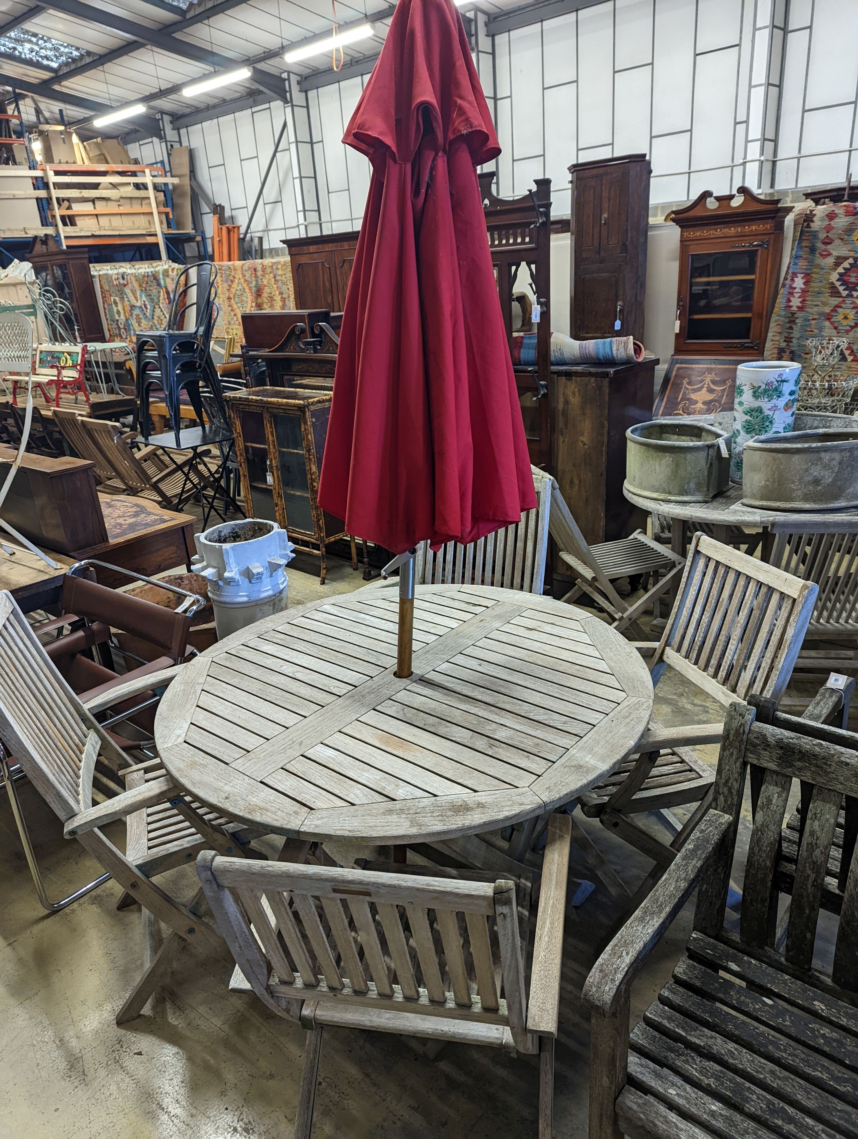 A circular weathered teak folding garden table, diameter 120cm, height 74cm, four folding elbow chairs and a parasol